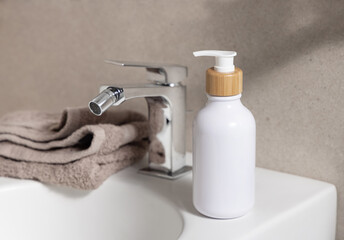 White one pump bottle and folded bath towel on basin against beige wall, cosmetic mockup