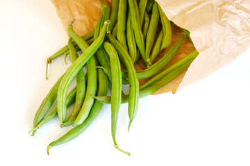 Closeup of organic ripe green bean pods in a brown paper eco bag on a white background. Zero waste...