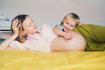 Pregnant mother and daughter together at home. Woman with her first child during second pregnancy. Motherhood and parenting concept. Toddler smiling girl and mom. Happy family expecting for new baby. - 792807196