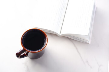 テーブルの上の開いた本とコーヒーカップで、コーヒーを飲みながら読書を楽しむイメージ
