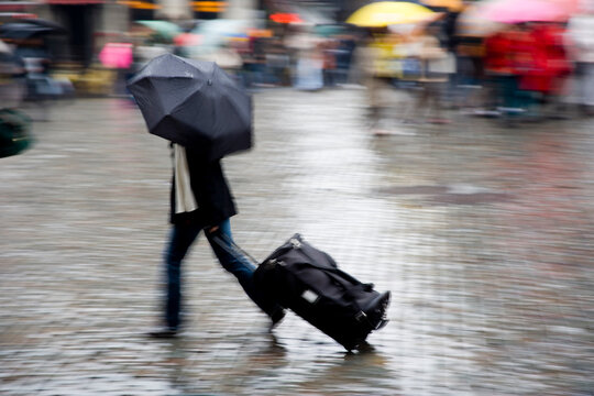 A solitary figure briskly moves through the rain with an umbrella, blurred in motion, evoking a sense of rush and resilience