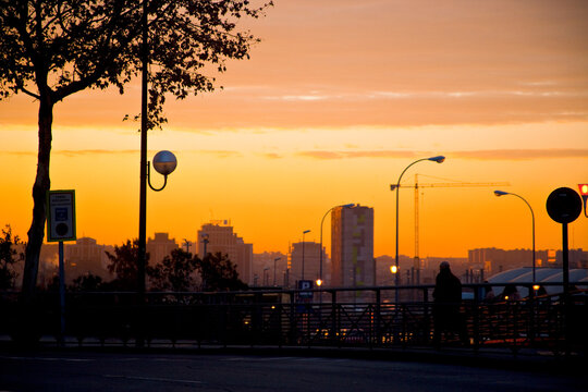 Warm orange hues fill the sky as the sunset casts a silhouette over the city, capturing the evening's ambiance