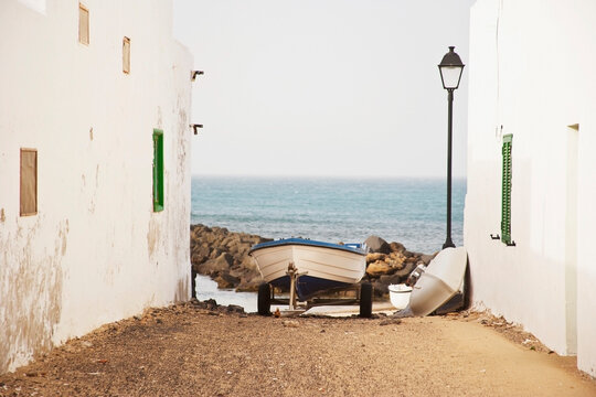 A picturesque scene capturing a small boat nestled between white rustic buildings leading to a tranquil ocean, invoking a sense of peace and simplicity
