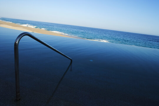 The solitary metal handrail on an empty pristine beach captivates the sense of solitude and contemplation against the ocean backdrop