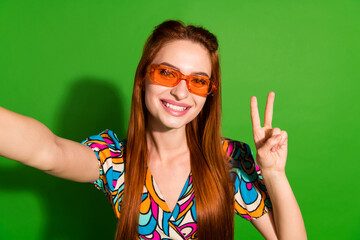 Photo portrait of attractive young woman sunglass selfie photo v-sign dressed stylish retro clothes isolated on green color background