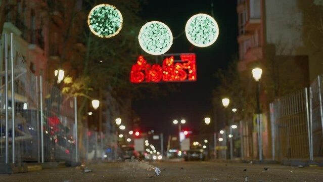 Teenage boy crouches lighting firecracker on urban street with background bokeh lights at night