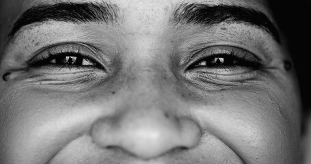 One young black woman smiling at camera, intense macro close-up detail person of African descent staring at camera with friendly happy demeanor in monochrome - obrazy, fototapety, plakaty