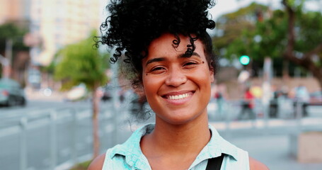 One happy young black woman of African Descent with curly hair standing in urban setting smiling....