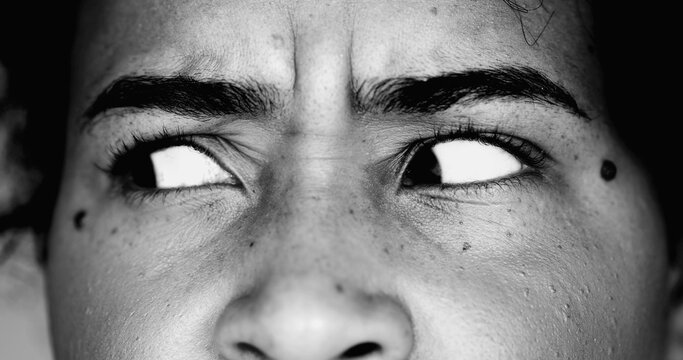 One paranoid worried young black woman macro close-up eyes looking sideways with intense preoccupation and obsession in dramatic black and white monochrome