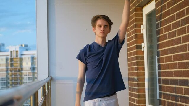Beginner slim guy athlete doing exercises on the balcony of a multi-story building
