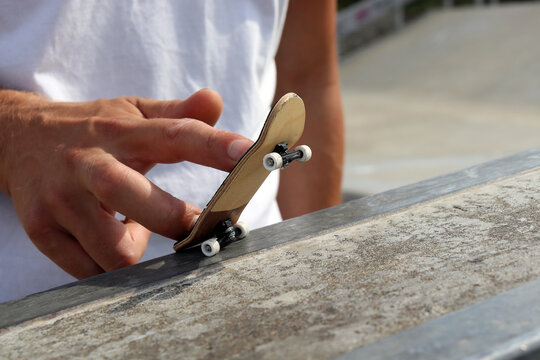 Male hand playing with black wooden fingerboard doing grind or slide trick at the ramp in skatepark, close up. Mini skateboard, small skateboard deck