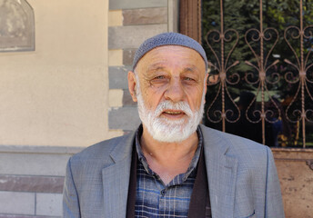 Serious grizzled Turkish retired old man with beard, beard and turban looking intently at his...