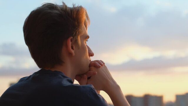 Young pensive man on the balcony at sunset