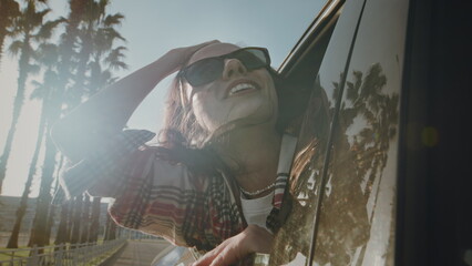 Female is enjoying a vacation in a city by the sea or ocean. Palm trees are reflected in the car