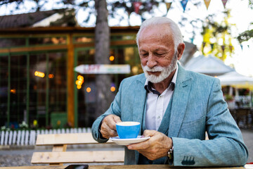 Thoughtful mature man drinking coffee in a cafe and looking away. Portrait of a bearded senior man...