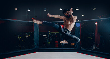 MMA Training of fighter without rules in octagon cage, man makes kick in flight on dark background