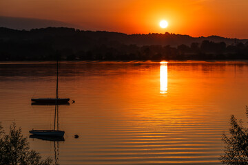 Romantyczny wschód słońca nad jeziorem z jachtem w tle
