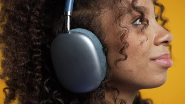 Positive african woman listening music, enjoying headphones, yellow background