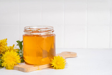 Dandelion jam, jelly confiture in a jar with fresh dandelion flowers on a white table background