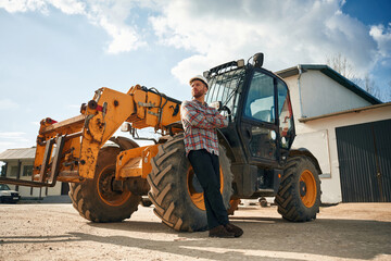 With arms crossed. Man is with tractor. Agricultural worker