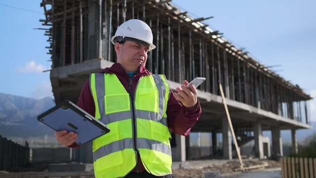 Tired engineer ends a nervous telephone conversation, cries, upset about the unsuccessful outcome of negotiations against the backdrop of a construction site.