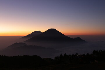 Sunrise on Mount Prau, Central Java, Indonesia. Golden rays appear on the blue horizon with mist...