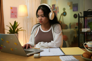 Teenage girl listening to music in headphones when studying at home