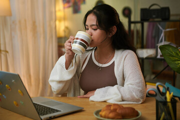 Teenage Vietnamese girl having tea with pastries when studying at home