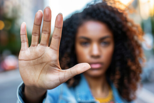 A focused African-American woman exhibits a stop symbol, holding her open palm towards the camera, indicating a halt, refusal, danger, rejection, or restriction with a hand gesture. 