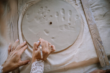 Valmiera, Latvia - August 10, 2023 - Hands carving into clay with footprints and handprints, on a...