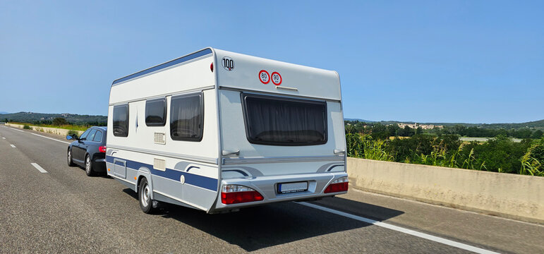 Car towing a caravan trailer on a freeway; automobile pulling a trailer camper on a quiet road in Spain on a sunny day.
