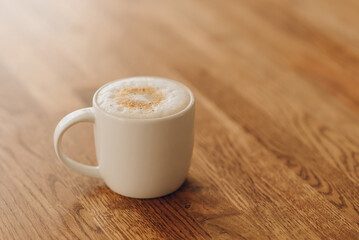 white mug with cappuccino on a wooden table, coffee with milk froth
