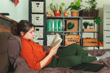 Beautiful young woman reading a book on the bed.