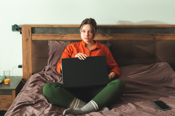 Beautiful young woman working on a laptop while sitting on a bed at home.