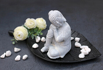 Sitzende Buddhafigur mit Blumen und Steinen.