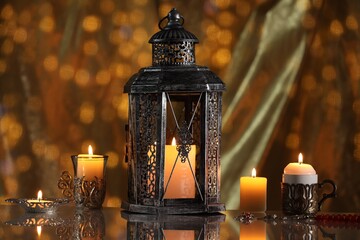 Arabic lantern and burning candles on mirror surface against blurred lights