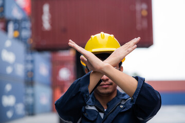 A man in a yellow helmet is holding his hands together in front of a container ship. Concept of...