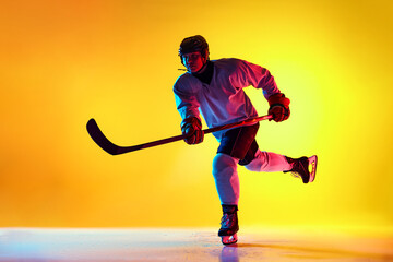 Dynamic image of male ice hockey player in mid-action on rink, shows his skills in neon light...