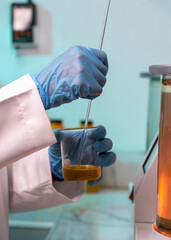 A person in a lab coat is stirring a yellow liquid in a beaker