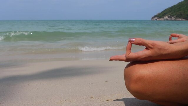 Closeup view on hands of woman practicing yoga in lotus pose on tropical sea beach. Meditation and zen