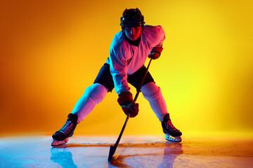 Dynamic portrait of hockey player, poised and ready for action in neon light against yellow...