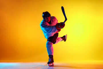 Dynamic photo of athletic player with stick training attack technique in neon light against yellow...