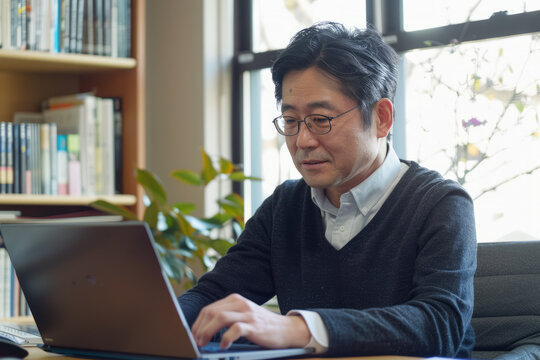 An experienced Japanese male therapist sits at his desk, immersed in his laptop, meticulously conducting research and reviewing clinical guidelines