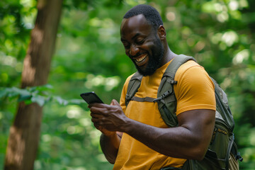 Outdoors, a cheerful black sportsman smiles as he texts on his cell phone, soaking in the tranquility of nature.