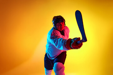 Focused ice hockey player in ready stance in neon light against gradient yellow background. Dynamic...