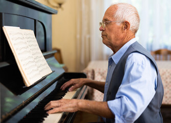 Grandfather is learning to play piano at home. Life after retirement concept - 792911523