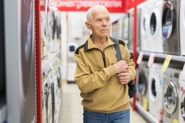 Elderly man choosing washing machine in showroom of electrical appliance store - 792911718