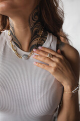 Young woman with a tattoo shows off jewelry on her neck and arm - a necklace with freshwater pearls...