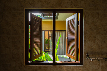 Wooden bathroom windows and shutters open revealing view of tropical plants and garden
