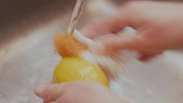 Woman fresh lemon with plastic brush, removing germs and pesticide residues from lemon skin with water. High quality 4k footage